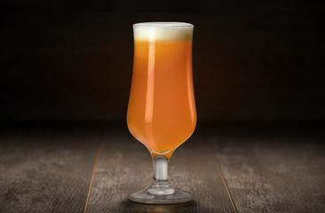 Delicious Golden Unfiltered India Pale Ale beer in tulip glass on reclaimed wooden table with black background