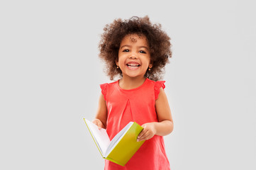 childhood, literature and reading concept - happy little african american girl with book over grey background