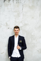 Fototapeta na wymiar Portrait of a handsome young groom in a stylish modern suit, standing against a white wall and smiling