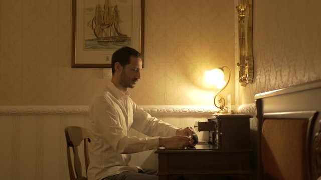 Man in white shirt takes out of a drawer his glasses, clean them and start writing.