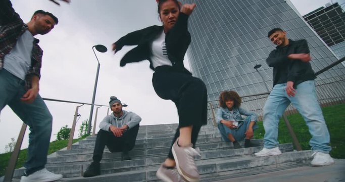 Slow motion of group of young urban dancers of different ethnicities are having fun to training in a city center with skyscrapers.