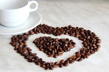 pure white Cup and saucer, lots of heart shaped coffee beans, close-up. coffee beans in the shape of a heart, after roasting on the table next to a white Cup, selective focus