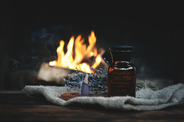 Magic potion bottle and dried lavender flower branches on a table on a burning fire background....