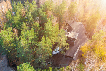 Aerial view of big modern luxuty cottage house between pine and birch trees in forest with boat on trailer parked at backyard