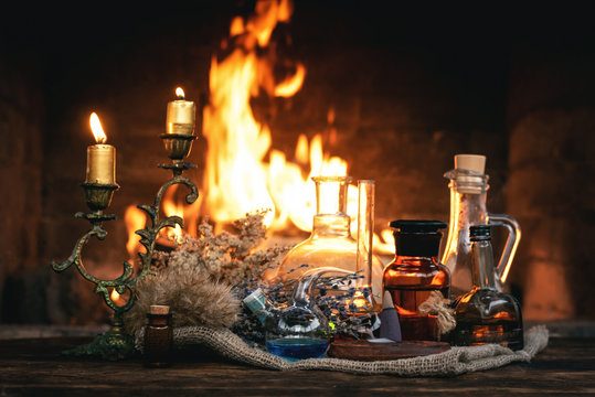 Alchemist table. Magic potion bottles and dried herbs on a table on a burning fire background. Witchcraft, witch doctor concept.