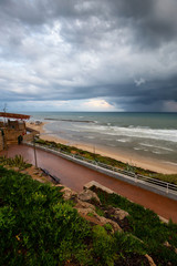 Fototapeta premium Beautiful view of a sandy beach during a cloudy sunrise. Taken in Netanya, Center District, Israel.