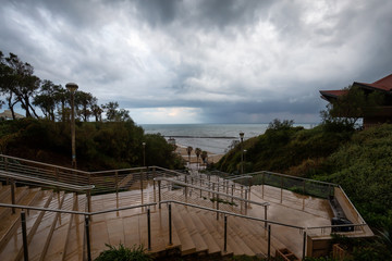Stairs going down to the sandy beach during a cloudy sunrise. Taken in Netanya, Center District, Israel.