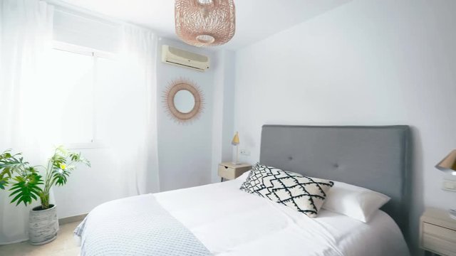 Comfortable hotel bedroom with felt headboard with natural fabric cushion, rattan lamp, wood nightstand and a big wooed wardrove.Holiday destination apartment with scandinavian style.