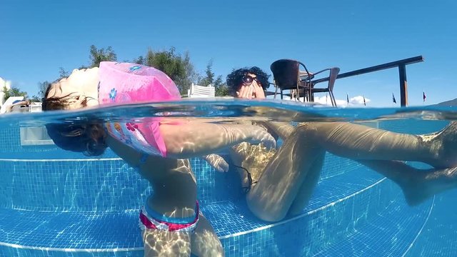 Family having fun swimming and refreshing in thermal spa pool, little girl with inflatable armbands floating on water surface, SLOW MOTION half underwater shot