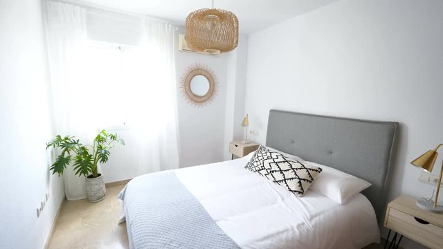Comfortable hotel bedroom with felt headboard with natural fabric cushion, rattan lamp, wood nightstand and a big wooed wardrove.Holiday destination apartment with scandinavian style.