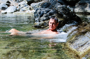 Gorge, mountains.  A young man swims along a mountain river in bright green color.  Summer, vacation, tourists.