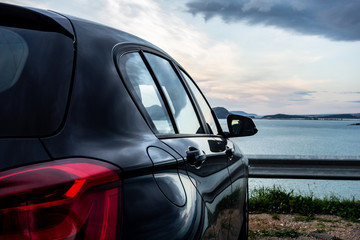 Rear view of modern luxury black car parked above the sea with a romantic view during the sunset - Powered by Adobe