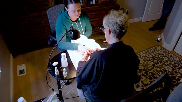 A manicurist or nail technician applies nail polish to a cute client