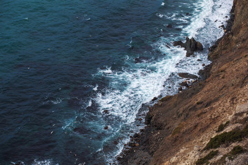 Obraz premium Rocky coast with sea waves and white foam at stone coastline, beautiful seascape background