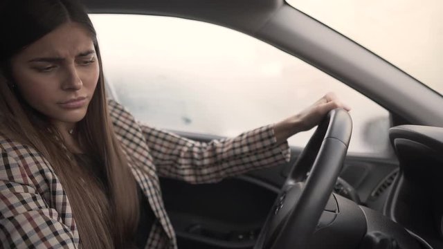 Beautiful young woman is going to drive a car but something is going wrong and she isn't able to start the car. Woman is absolutely disappointed and frustrated.