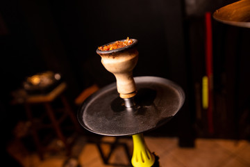 wooden hookah bowl filled with orange tobacco against a black wall