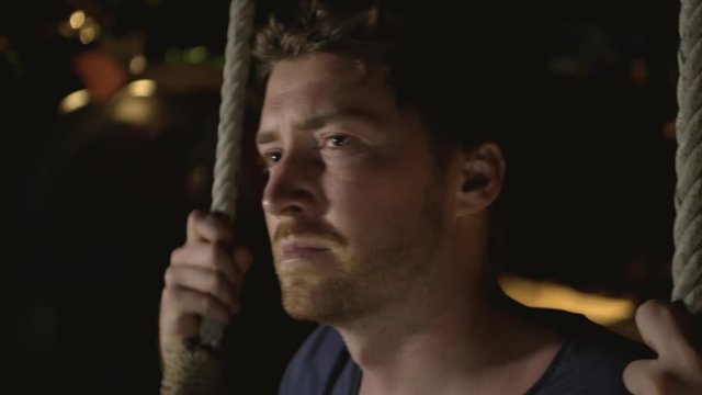 A contemplative man lightly swinging at night