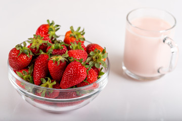 Fresh strawberry in a bowl and glass of milk on wooden background.