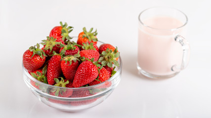 Fresh strawberry in a bowl and glass of milk on wooden background.