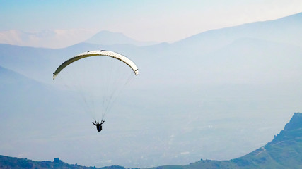 Paraglider silhouette fly over the mountain valley