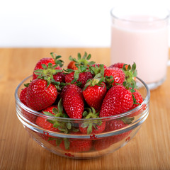 Fresh strawberry in a bowl and glass of milk on wooden background.