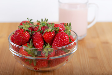 Fresh strawberry in a bowl and glass of milk on wooden background.
