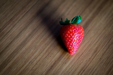 Red trawberry with green leaves stands on a wood table with marked lines