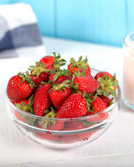Fresh strawberry in a bowl and glass of milk on wooden background.