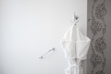 Close up of white clean bathrobe hanging on a hanger. Luxury modern interior of stylish and elegant bathroom in hotel. Private apartment. Minimalistic design in light shades