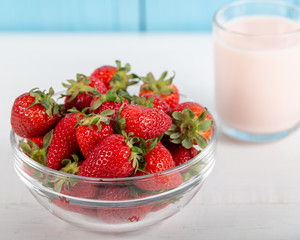 Fresh strawberry in a bowl and glass of milk on wooden background.