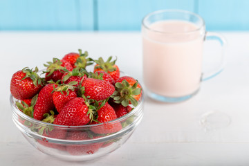Fresh strawberry in a bowl and glass of milk on wooden background.