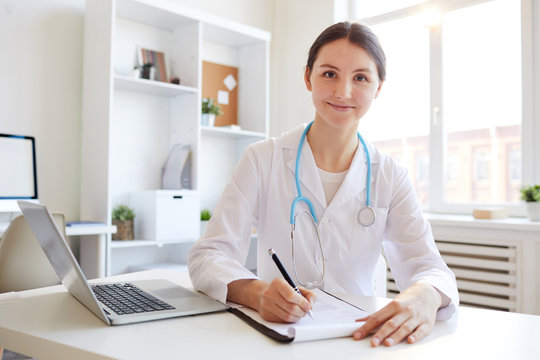 Portrait of young female doctor smiling at camera while working in office, copy space