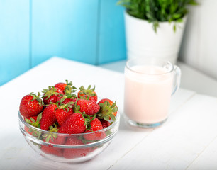 Fresh strawberry in a bowl and glass of milk on wooden background.