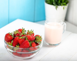 Fresh strawberry in a bowl and glass of milk on wooden background.
