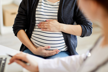 Closeup of unrecognizable woman gently holding prengnant belly during consultation with obstetrician, copy space