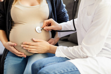 Closeup of unrecognizable obstetrician listening to baby heartbeat putting sthetoscope to pregnant...