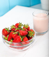 Fresh strawberry in a bowl and glass of milk on wooden background.