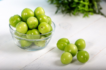 Green plums in glass bowl on wooden table 