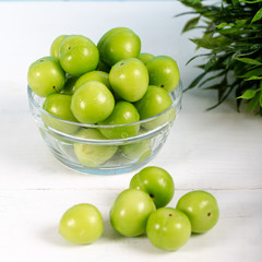 Green plums in glass bowl on wooden table 