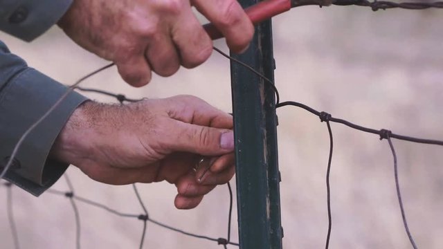 Slow motion close up detail of a male farmer's hands twisting new wire on a metal fence stay in West, Texas, 29.97 fps, 4K.