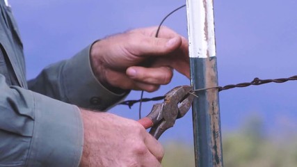 Slow motion close up of male hands using pliers to tighten and twist new wire onto a farm fence in West, Texas, 29.97 fps, 4K.