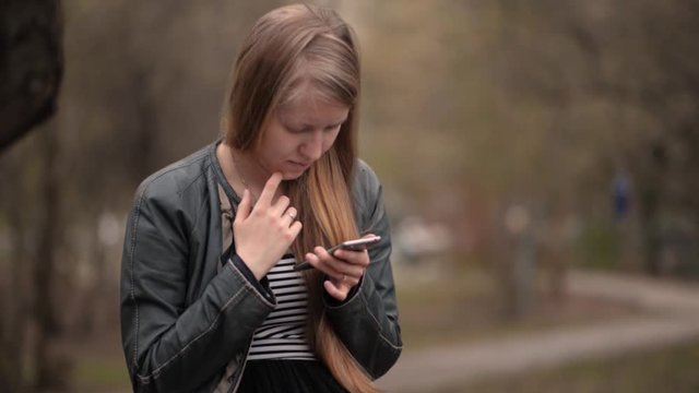 Beautiful blonde young girl looking at smartphone cloud day halfbody portrait
