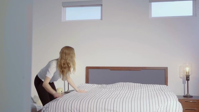 Slow motion shot of a girl fixing her bed in the morning, smoothening the duvet, 29.97 fps.