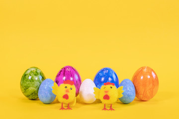Seven colored Easter eggs on a yellow background. Easter eggs stand in a row. In the foreground are yellow chicks. Happy Easter card  with free, empty space.