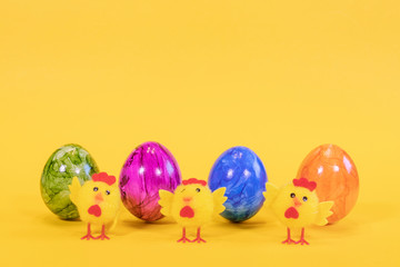 Fototapeta na wymiar Four colored Easter eggs on a yellow background. Easter eggs stand in a row. In the foreground are yellow chicks. Happy Easter card with free, empty space.