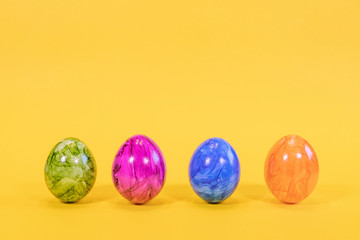 Fototapeta na wymiar Four colored Easter eggs on a yellow background. Easter eggs stand in a row. Happy Easter card with free, empty space.
