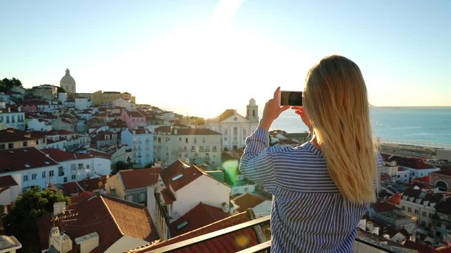 A Girl is taking a photo of the sunrise over Alfama in Lisbon, Portugal.