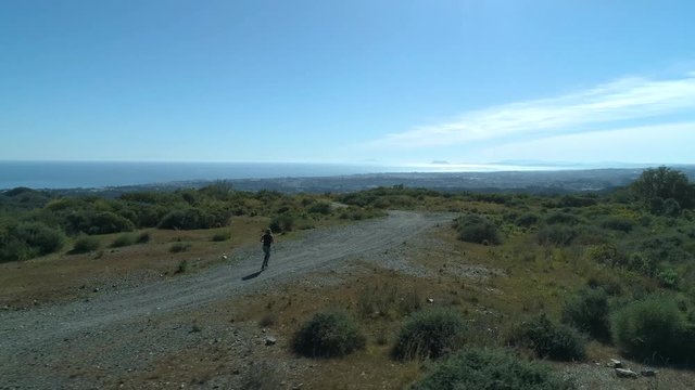 Drone follows blonde woman jogging in the mountains.