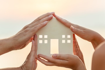 A close up of a small house figure, held by five human hands in a circle