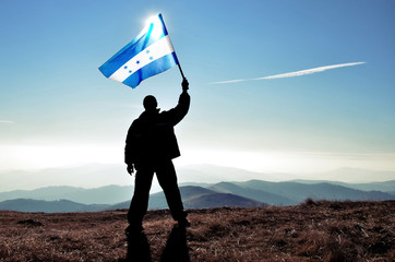 Successful silhouette man winner waving Honduras flag on top of the mountain peak